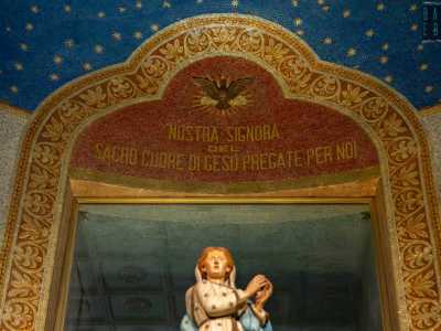 Al centro una ricca cornice vegetale custodisce un mosaico rosso con scritta dorata e piccolo vano che un tempo ospitava il gruppo statuario del Cuore di Maria affiancato dai santi Benedetto e Scolastica